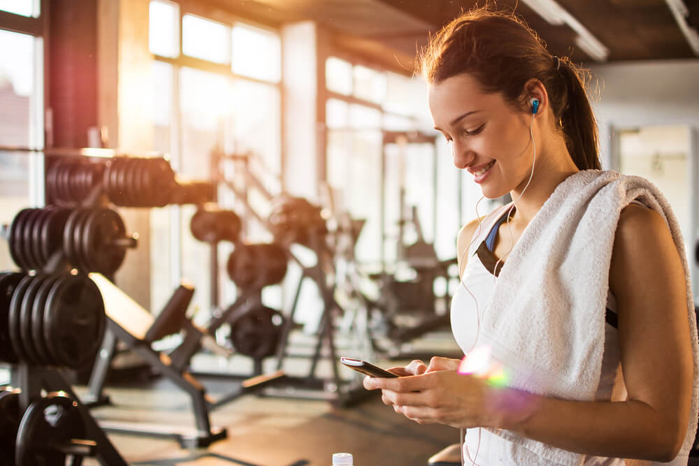 Girl in gym looking at phone and smiling -best gyms in nottingham