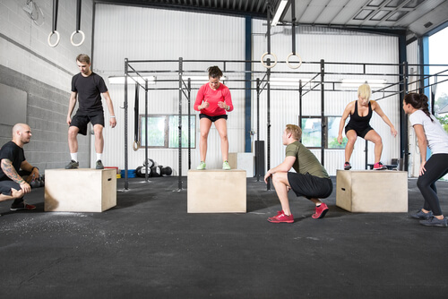 2 girls and one man , with a personal trainer jumping on boxes in a gym - cross fit 