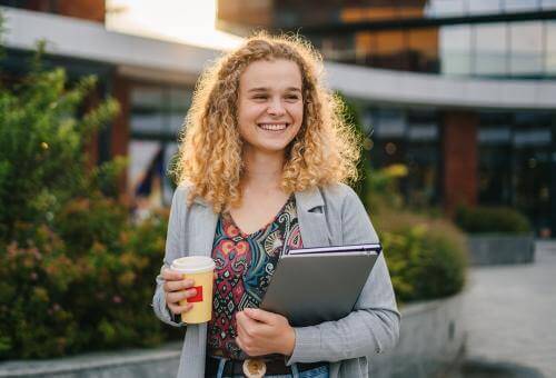 Girl holding a book and coffee and smiling 